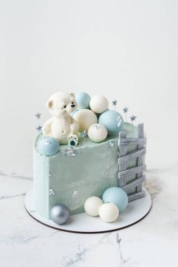 Üzerinde oyuncak ayıyla süslenmiş mavi çikolata kaplı pastanın son moda yarısı. Beyaz arka planda çikolata turkuazlı ve gümüş küreli küçük bir bebek için doğum günü pastası. 6 aylık kutlama.