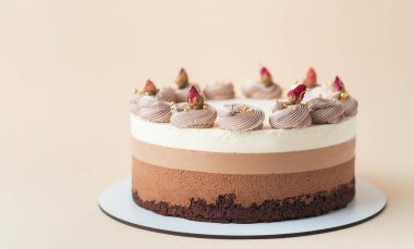 Bej arka planda üç tane ev yapımı kek. Süngerli çikolatalı sufle kek ve çırpılmış krema ve kurutulmuş çiçeklerle süslenmiş üç kat çikolatalı mus.