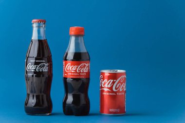 Kyiv, Ukrayna - 09 Ocak 2025: Mavi arka planda cam, plastik şişeler ve Coca-Cola meşrubatları. Coca-Cola Amerika 'dan ünlü bir marka. Şeker tüketimi ve geri dönüşüm kavramı