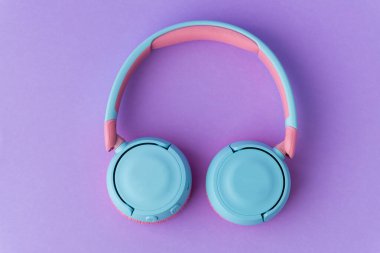 Mor arka planda parlak pembe ve mavi kablosuz kulaklıklar. Müzik ve teknoloji konsepti. Kopyalama alanı ile yakın çekim