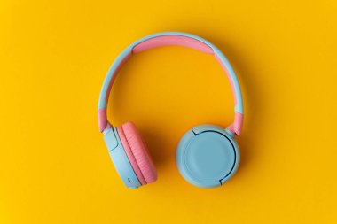 Sarı arka planda parlak pembe ve mavi kablosuz kulaklıklar. Müzik ve teknoloji konsepti. Kopyalama alanı ile yakın çekim