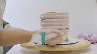 Pasta şefinin pasta tezgahını krem peynirle süslediği pasta poşeti ve spatulayla kapatmasını. Şekerlemecinin pastayı birleştirip süsleme süreci