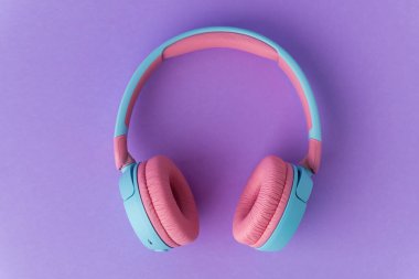 Mor arka planda parlak pembe ve mavi kablosuz kulaklıklar. Müzik ve teknoloji konsepti. Kopyalama alanı ile yakın çekim
