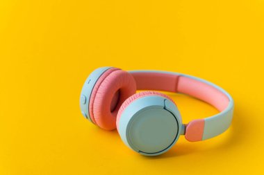 Sarı arka planda parlak pembe ve mavi kablosuz kulaklıklar. Müzik ve teknoloji konsepti. Kopyalama alanı ile yakın çekim