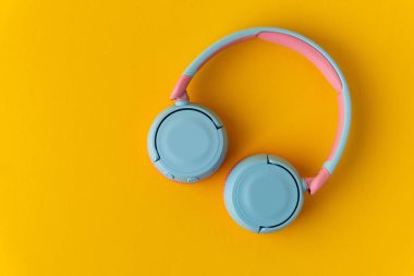 Sarı arka planda parlak pembe ve mavi kablosuz kulaklıklar. Müzik ve teknoloji konsepti. Kopyalama alanı ile yakın çekim
