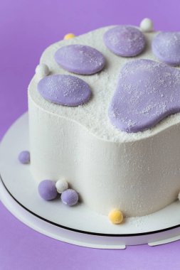Mor arka planda modaya uygun, yumuşak, yumuşak patili bir doğum günü pastası. Beyaz krem peynirli kremalı bir çocuk için Taba pençesi şeklinde pasta.