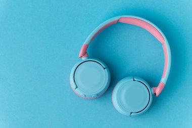 Mavi arka planda parlak pembe ve mavi kablosuz kulaklıklar. Müzik ve teknoloji konsepti. Kopyalama alanı ile yakın çekim