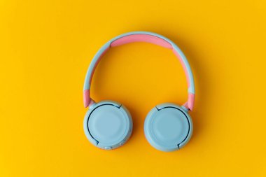 Sarı arka planda parlak pembe ve mavi kablosuz kulaklıklar. Müzik ve teknoloji konsepti. Kopyalama alanı ile yakın çekim