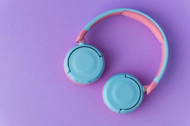 Mor arka planda parlak pembe ve mavi kablosuz kulaklıklar. Müzik ve teknoloji konsepti. Kopyalama alanı ile yakın çekim