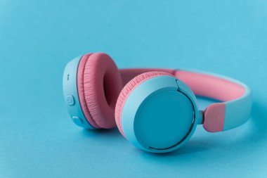 Mavi arka planda parlak pembe ve mavi kablosuz kulaklıklar. Müzik ve teknoloji konsepti. Kopyalama alanı ile yakın çekim
