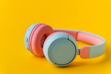 Sarı arka planda parlak pembe ve mavi kablosuz kulaklıklar. Müzik ve teknoloji konsepti. Kopyalama alanı ile yakın çekim