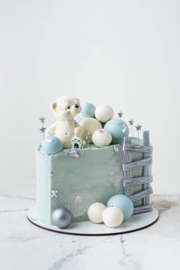 Üzerinde oyuncak ayıyla süslenmiş mavi çikolata kaplı pastanın son moda yarısı. Beyaz arka planda çikolata turkuazlı ve gümüş küreli küçük bir bebek için doğum günü pastası. 6 aylık kutlama.