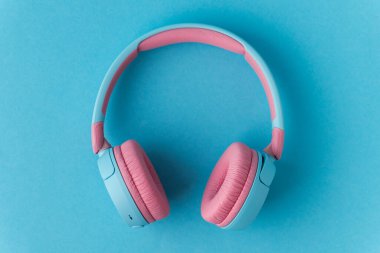 Mavi arka planda parlak pembe ve mavi kablosuz kulaklıklar. Müzik ve teknoloji konsepti. Kopyalama alanı ile yakın çekim