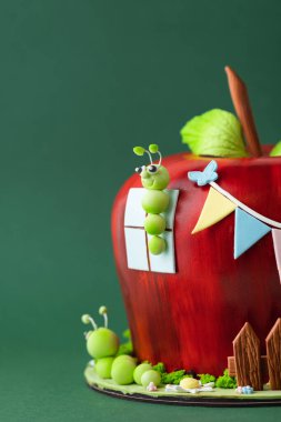 Red apple shaped fondant cake decorated with mastic edible caterpillar, green leaves and moss. Green background. Orchard fruits themed birthday cake clipart