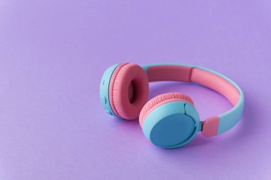 Mor arka planda parlak pembe ve mavi kablosuz kulaklıklar. Müzik ve teknoloji konsepti. Kopyalama alanı ile yakın çekim
