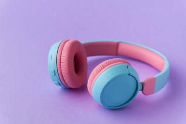 Mor arka planda parlak pembe ve mavi kablosuz kulaklıklar. Müzik ve teknoloji konsepti. Kopyalama alanı ile yakın çekim