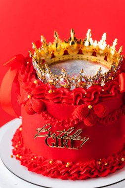Güzel kraliçe ya da prenses temalı kırmızı pasta. Şatafatlı Lambeth tarzı doğum günü pastası klasik krema izi ve altın tacıyla süslenmiş. Kırmızı arkaplan.