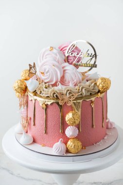 Güzel lüks doğum günü pastası pembe çikolata kremalı altın renkli çikolata damlaları ve beyaz arka planda altın şekerlerle süslenmiş.