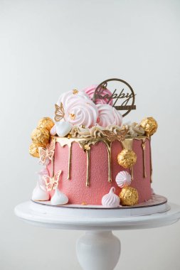 Güzel lüks doğum günü pastası pembe çikolata kremalı altın renkli çikolata damlaları ve beyaz arka planda altın şekerlerle süslenmiş.