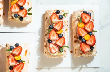 Beyaz arka plandaki sert ışığın altında badem taneli kremalı kremalı pasta rulosu. Çilek ve yaban mersinli yumuşak kremalı Pavlova yaz tatlısı.