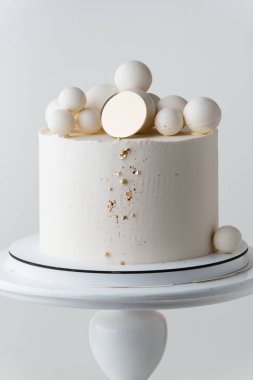 Çikolata küreleri ve altın parçacıklarla süslenmiş beyaz çikolata kaplı güzel bir düğün pastası. Beyaz arkaplan