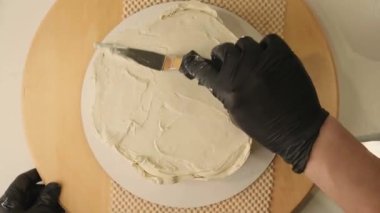 Pasta şefinin pasta tezgahını krem peynirle süslediği pasta poşeti ve spatulayla kapatmasını. Şekerlemecinin pastayı birleştirip süsleme süreci