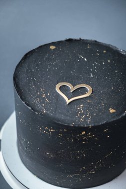 Üzerinde altın spreyler ve altın kalp siluetiyle süslenmiş siyah çikolatalı pasta. Sevilen biri için şık bir pasta. Koyu gri arkaplanda Sevgililer Günü pastası