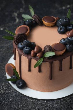 Siyah arka planda yaban mersinli, kurabiyeli ve şekerli çikolatalı pasta. Kahverengi krem peynirli pasta ve üzerinde koyu çikolata damlaları.