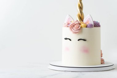 Tatlı tek boynuzlu at temalı pasta beze çiçekleri ve beyaz arka planda altın boynuz ile süslenmiş. Bir kız için güzel, uzun bir doğum günü pastası