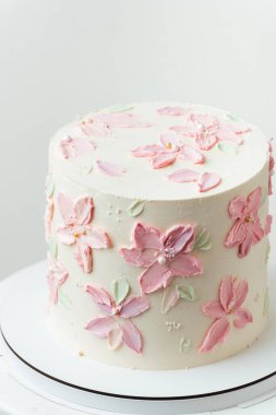 Doğum günü, düğün ya da yıldönümü pastası beyaz krem peynirle kaplanmış ve pembe krem çiçek yapraklarıyla süslenmiş. Beyaz arkaplan
