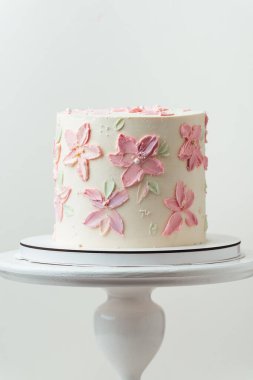 Doğum günü, düğün ya da yıldönümü pastası beyaz krem peynirle kaplanmış ve pembe krem çiçek yapraklarıyla süslenmiş. Beyaz arkaplan