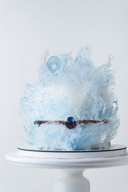 Yüzücü silueti olan güzel bir pasta. Yenilebilir su dalgaları ve karamelli ya da izomaltla süslenmiş kek. Olimpik yüzme şampiyonu için doğum günü pastası. Beyaz arkaplan