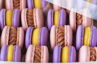 Beyaz mermer arka plandaki karton kutudaki çok renkli badem kurabiyelerini kapat. Sarı çikolatalı pembe ve menekşe badem kurabiyesi çeşitleri. Hediye kutusunda ünlü Fransız tatlıları.