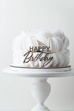 Beyaz yenilebilir kağıt yapraklarla kaplı doğum günü pastası ve altın doğum günü süsü ile süslenmiş. Beyaz arkaplan
