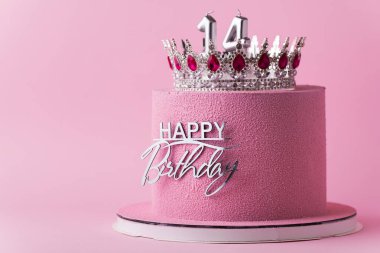 Gümüş taç ve doğum günü süsü ile süslenmiş pembe çikolata kadife kaplamalı güzel bir doğum günü pastası. Pembe arka plan. Mutlu 14 yıllık kutlama konsepti