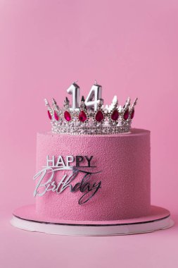 Gümüş taç ve doğum günü süsü ile süslenmiş pembe çikolata kadife kaplamalı güzel bir doğum günü pastası. Pembe arka plan. Mutlu 14 yıllık kutlama konsepti