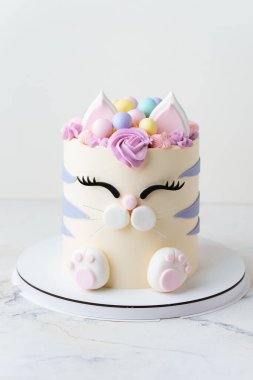 Beyaz arka planda pembe krem kürkle süslenmiş mastik kulaklı ve pençeli kedi şeklinde şirin bir doğum günü pastası. Kedileri seven küçük bir kız için sevimli bir pasta.