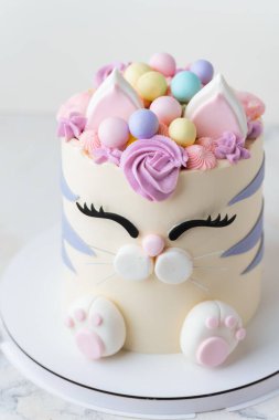 Beyaz arka planda pembe krem kürkle süslenmiş mastik kulaklı ve pençeli kedi şeklinde şirin bir doğum günü pastası. Kedileri seven küçük bir kız için sevimli bir pasta.
