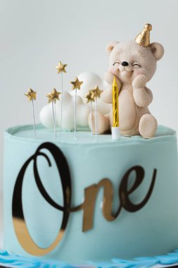 Çikolata kaplı, oyuncak ayı ve beyaz bulutlarla süslenmiş mavi çikolata kaplı bir bebek için doğum günü pastası. Turkuaz arka planda küçük bir çocuk için bebek partisi pastası.