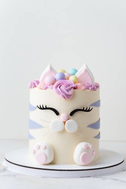 Beyaz arka planda pembe krem kürkle süslenmiş mastik kulaklı ve pençeli kedi şeklinde şirin bir doğum günü pastası. Kedileri seven küçük bir kız için sevimli bir pasta.