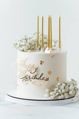 Beyaz arka planda altın mumlarla süslenmiş güzel beyaz doğum günü pastası ve çayırda çıngıraklı yılan çiçekleri.