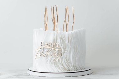 Beyaz çikolatalı lüks doğum günü pastası ve yenilebilir kağıtla süslenmiş şekerleme ve beyaz arka planda altın mumlar. Bir bayan için güzel beyaz yıldönümü pastası