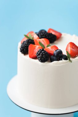 Taze ahududu ve böğürtlenlerle süslenmiş beyaz krem peynirli doğum günü pastası. Mavi arka planda kırmızı ve siyah böğürtlenli zarif yaz pastası