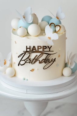 Çikolata küreleri ve yenilebilir kelebeklerle süslenmiş beyaz çikolata kaplı güzel bir doğum günü pastası. Beyaz arkaplan