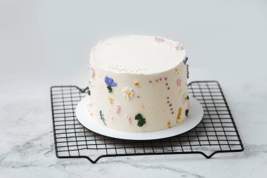 Gri pastel arka planda krema çiçekleriyle süslenmiş beyaz çikolata kremalı güzel bir doğum günü pastası.