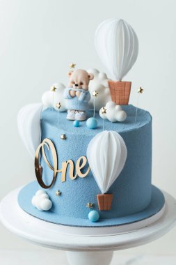Mavi çikolata kadife kaplamalı doğum günü pastası ve üzerinde yenebilir oyuncak ayı figürü ve balonlarla süslenmiş. Beyaz arka planda küçük bir çocuk için şirin bir doğum günü pastası.