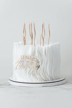 Beyaz çikolatalı lüks doğum günü pastası ve yenilebilir kağıtla süslenmiş şekerleme ve beyaz arka planda altın mumlar. Bir bayan için güzel beyaz yıldönümü pastası