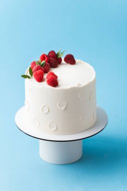 Taze ahududu ve böğürtlenlerle süslenmiş beyaz krem peynirli doğum günü pastası. Mavi arka planda kırmızı ve siyah böğürtlenli zarif yaz pastası