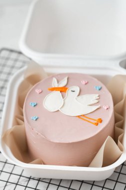 Bebek taşıyan leyleğin çikolata figürüyle süslenmiş pembe çikolata kaplı küçük bir kıza doğum günü pastası. Beyaz arka planda hediye kutusunda bir bebek partisi için pasta.