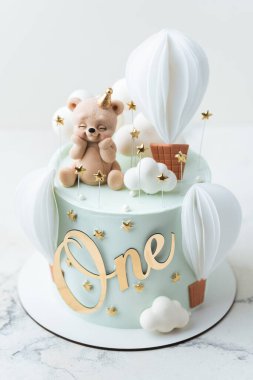 Turkuaz çikolata kadife kaplamalı doğum günü pastası ve üzerinde yenebilir oyuncak ayı figürü ve balonlarla süslenmiş. Beyaz arka planda küçük bir çocuk için şirin bir doğum günü pastası.